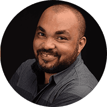 Smiling Black man with a beard and short hair, wearing a grey button-down shirt.